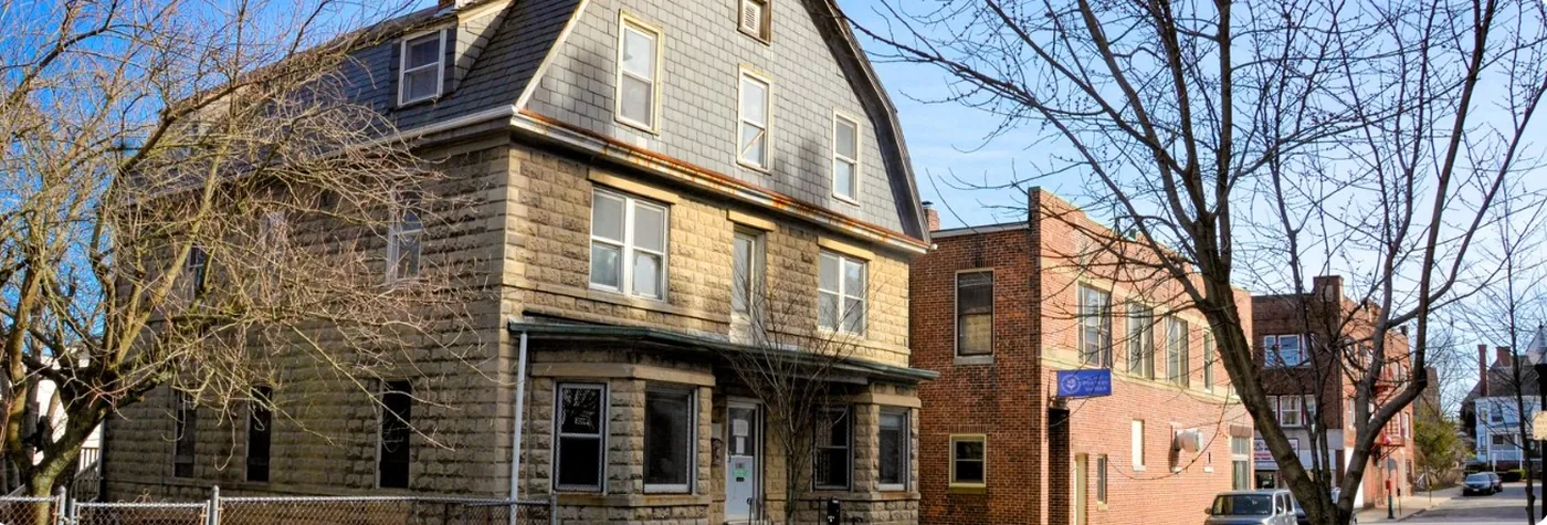 A three-story stone and shingle house on a downtown New Bedford corner, beside a brick building, under bare winter trees