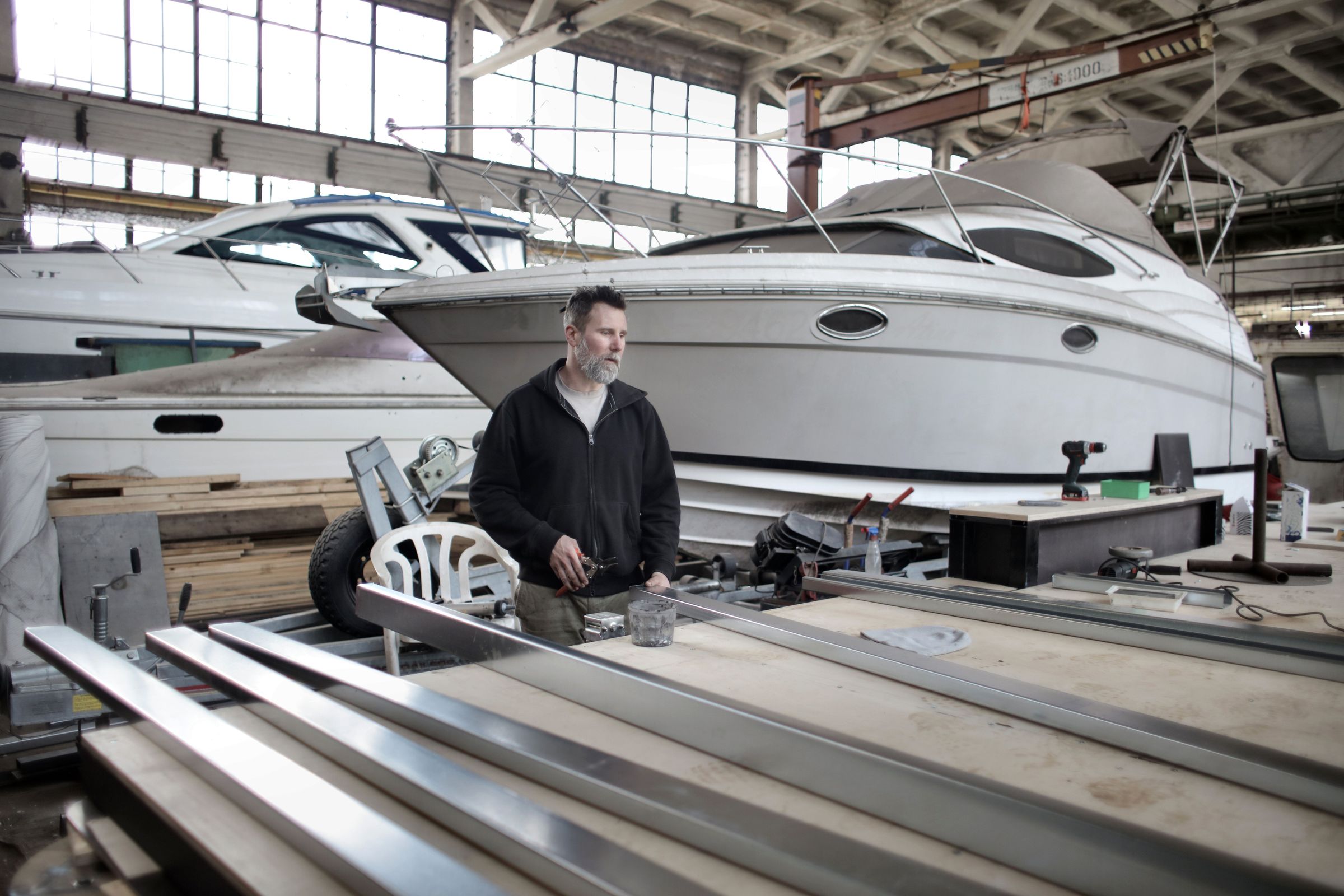 A boat mechanic at a workbench in a large workshop, with a motor yacht on a stand beside him