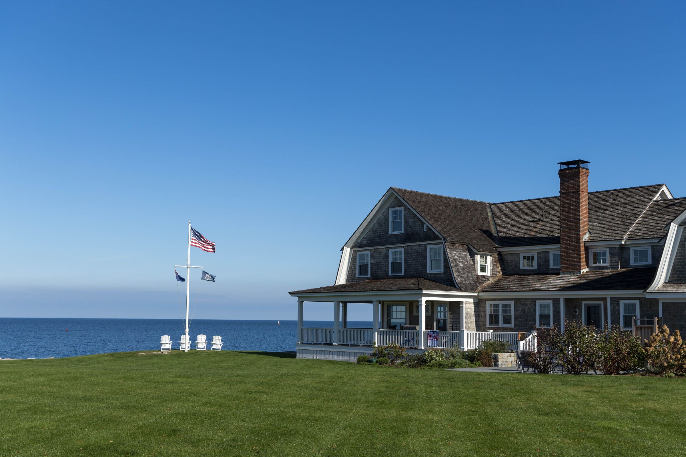 A shingle-style house on the Connecticut shore with a flag on the lawn and open water behind